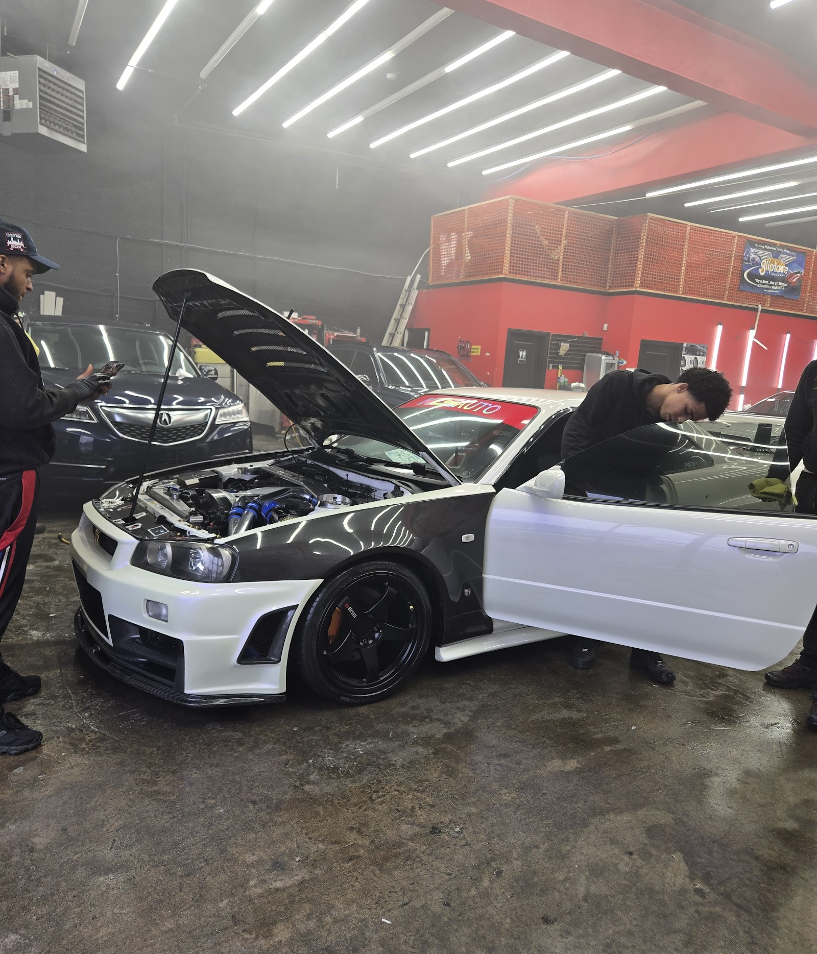 Sports sedan on the bay floor with hood up, detailers at work